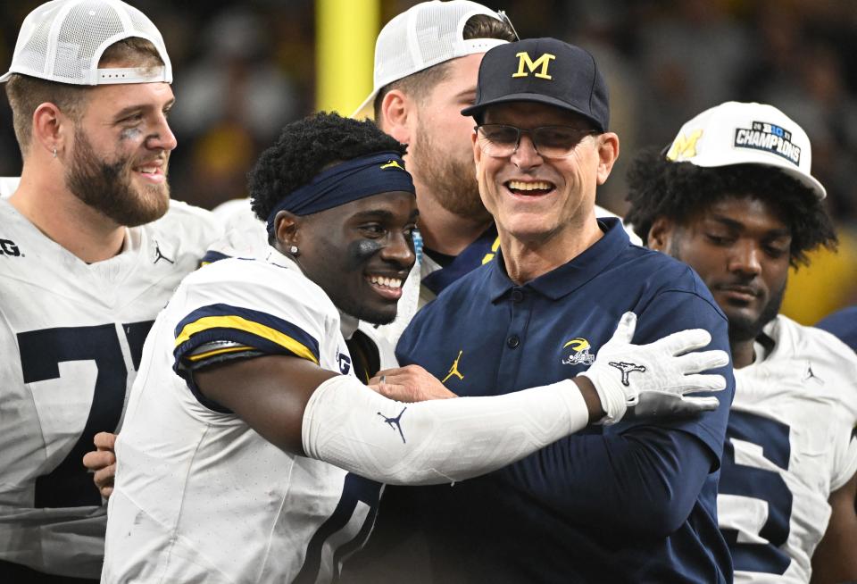 Michigan coach Jim Harbaugh celebrates with defensive back Mike Sainristil (0) after winning the Big Ten championship game against Iowa at Lucas Oil Stadium.
