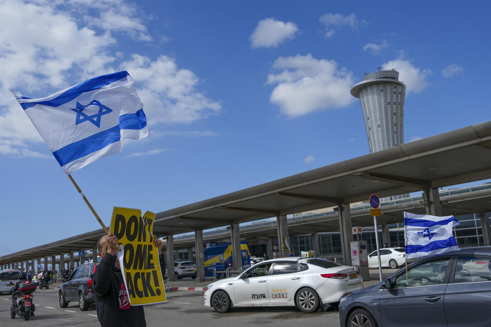 A man holds a sign , don't come back, and an Israeli flag during protest against plans by Prime Minister Benjamin Netanyahu's government to overhaul the judicial system, ahead of Netanyahu's visit to Germany in Ben Gurion airport near Tel Aviv, Israel, Wednesday, March 15, 2023. Hundreds of Israeli writers, artists and intellectuals on Tuesday called on Germany and Britain to cancel upcoming visits by Prime Minister Benjamin Netanyahu, saying his plan to overhaul Israel's judicial system has put the country on a destructive course. (AP Photo/Tsafrir Abayov)