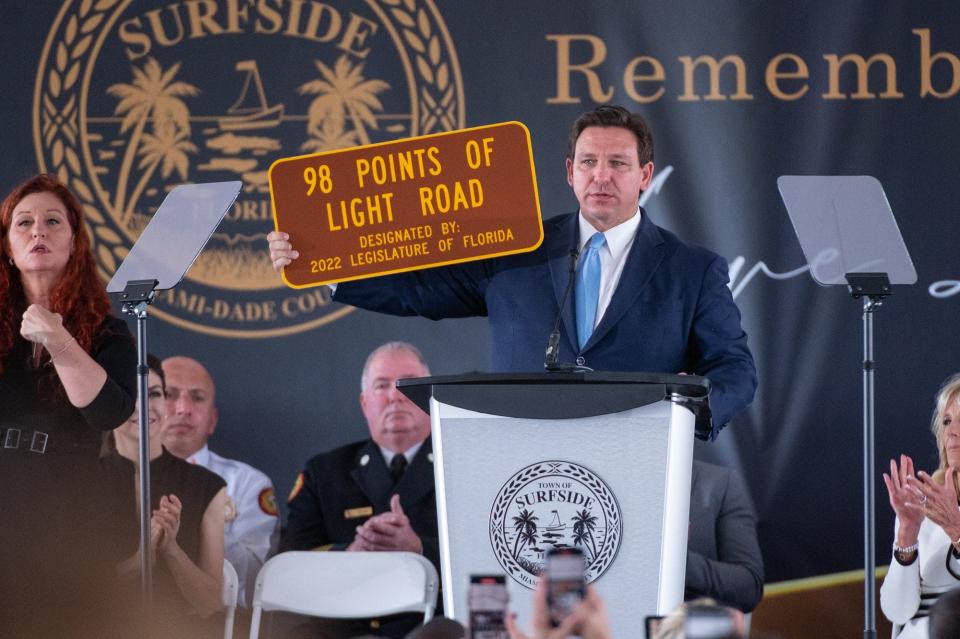 Florida Gov. Ron DeSantis holds up a sign signaling the new designation of the road by the former location of the Champlain Towers South condo in Surfside, on Friday, June 24, 2022. Hundreds attended a public memorial in honor of the 98 victims at the former site of the towers. Friday marked the one-year anniversary of the tragedy.