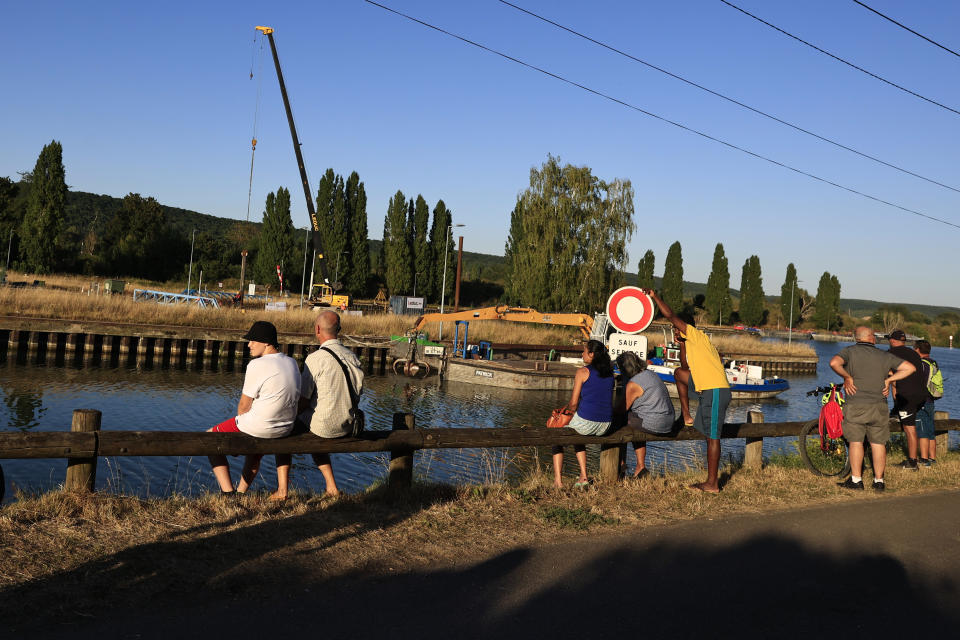 Onlookers wait near the lock of Notre Dame de la Garenne where a Beluga whale is being prepared to be moved, in Saint-Pierre-la-Garenne, west of Paris, France, Tuesday, Aug. 9, 2022. French environmentalists are moving a dangerously think Beluga that had strayed into the Seine River last week to a salt-water river basin to try and save its life. Lamya Essemlali, president of Sea Shepherd France, said the ethereal white mammal measuring 4-meters will be transported to the salty water for "a period of care" by medics who suspect the mammal is sick. (AP Photo/Aurelien Morissard)