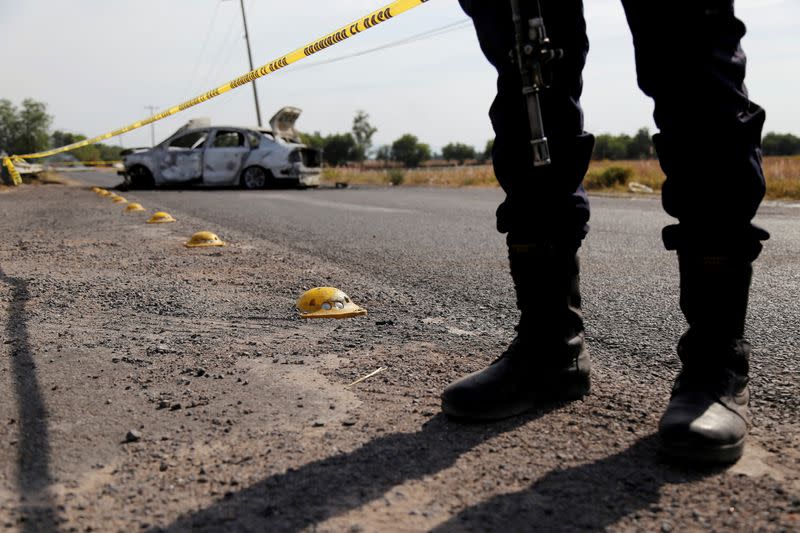 A policeman keeps watch near the wreckage of a car that was burnt in a blockade set by members of the Santa Rosa de Lima Cartel to repel security forces during a police operation on the outskirts of Celaya