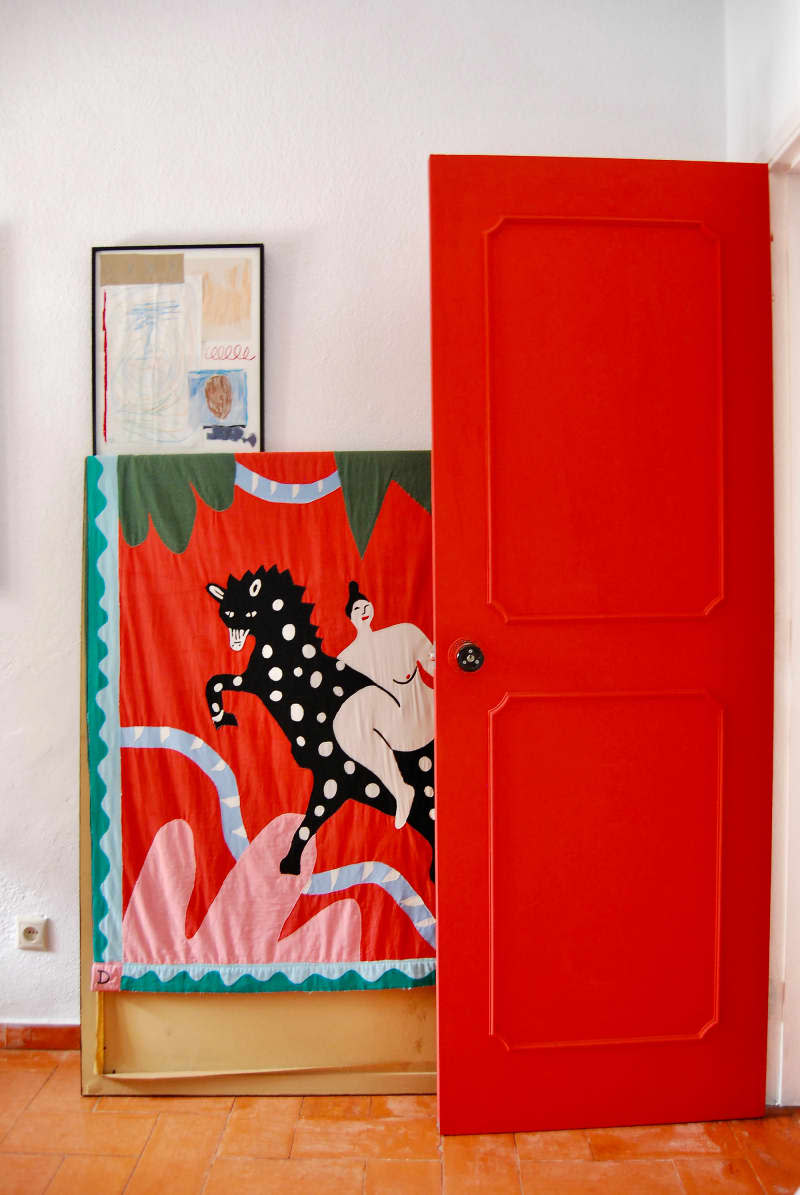 Red tapestry artwork behind red door in white room.