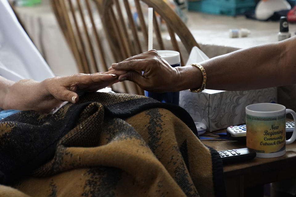 Louise Billiot, right, admires the nails of Vorina Roussell, who is bed-bound from a stroke, inside a trailer she is living in with her sister-in-law IreneVerdin, next to her home that was heavily damaged by Hurricane Ida nine months before, along Bayou Pointe-au-Chien, La., Tuesday, May 24, 2022. (AP Photo/Gerald Herbert)