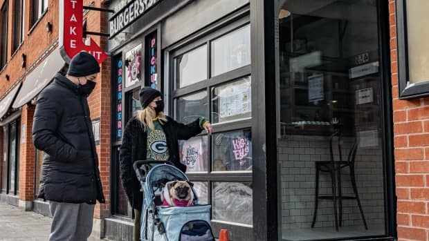 A couple pushing a pug in a stroller checks out the menu of a restaurant in downtown Ottawa. Scientists warn the city's COVID-19 numbers could easily increase if people aren't careful, especially with new variants making their way across the province.