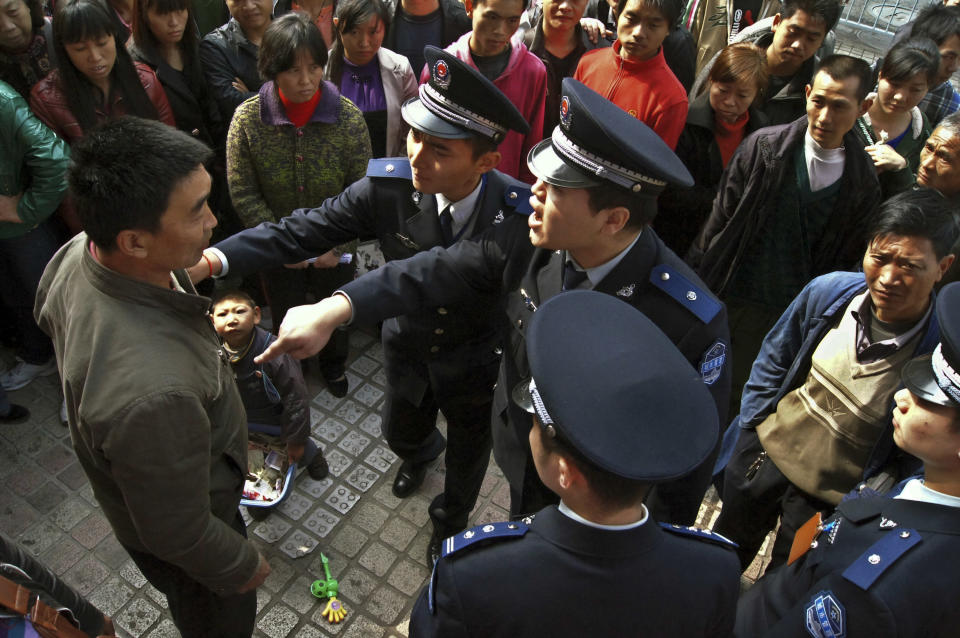 In this Nov. 20, 2011 photo, officers of the urban management bureau, known as chengguan in Chinese, demand a beggar and his child to leave a street in Guiyang, in southwestern China's Guizhou province. The urban management bureau, a branch of city governments that China set up to monitor everything from unlicensed street vendors to unauthorized construction, is rife with abuse of power, stoking already high social tensions, a rights group said Wednesday. (AP Photo) CHINA OUT