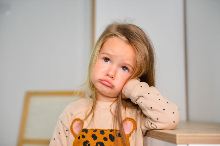 Young child looking upset with their cheek resting on hand