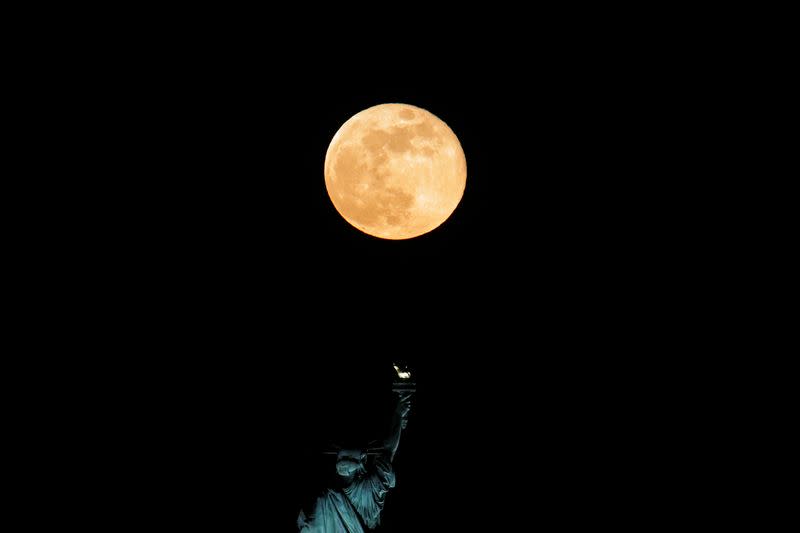 FILE PHOTO: The full moon also known as the Supermoon or Flower Moon rises above the Statue of Liberty as seen from Jersey City