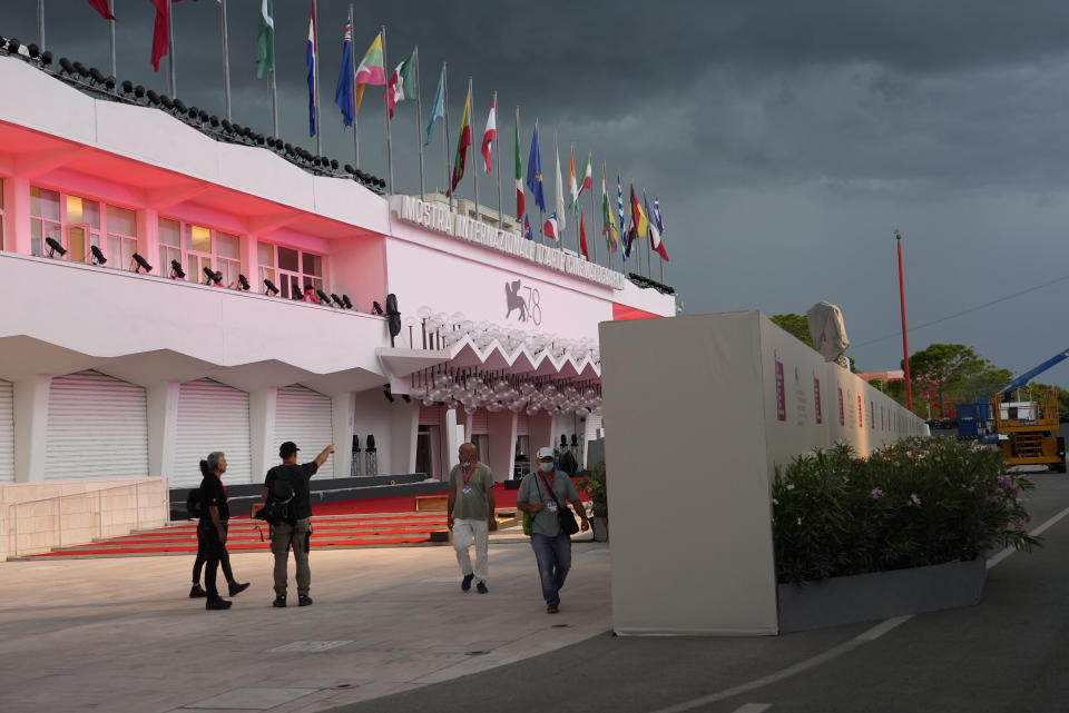 Workers walk by a wall hiding the red carpet of the 78th edition of the Venice Film Festival from the view of the public at the Venice Lido, Italy, Monday, Aug. 30, 2021. (AP Photo/Domenico Stinellis)