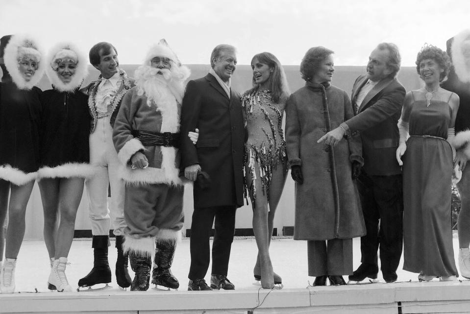 FILE - President Jimmy Carter calls for other performers to join himself, Santa Claus and ice skating star Peggy Fleming for pictures at a White House reception for U.S. Secret Service agents and military aides in Washington, Dec. 22, 1980. Jill Biden is bringing a holiday ice rink to the White House lawn for children to skate and play hockey during the holidays. The first lady was set to announce the rink after sunset on Wednesday. She was to be joined by 1988 Olympic figure skater Brian Boitano and the Snoopy character, among others. The White House says the rink will operate during December. (AP Photo/Dennis Cook, File)