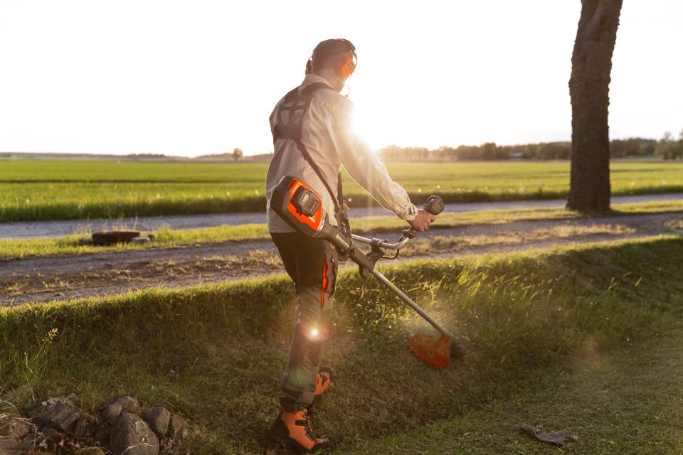 man with a brush cutter cutting the lawn on a bank