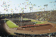 FILE - In this Oct. 10, 1964, file photo, balloons fly over Olympians and spectators during the opening ceremony of the 1964 Summer Olympics at the National Stadium in Tokyo. Every Japanese of a certain age has memories of the 1964 Tokyo Olympics. Even younger Japanese have connections through parents or aunts and uncles who saved old photos, faded certificates, or recall getting a television for the first time to watch the Games. (AP Photo, File)