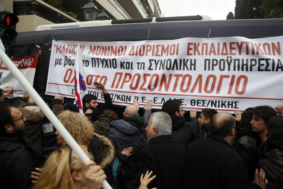 Teachers and other protesters push police buses during clashes near the Prime Minister's office in Athens, Friday, Jan. 11, 2019. About 1,500 people took part in the protest. Teachers' unions oppose the government's selection process for the planned hiring of 15,000 new teachers over the next three years. The banner reads ''Mass Full Time Hiring for Teachers.'' (AP Photo/Thanassis Stavrakis)