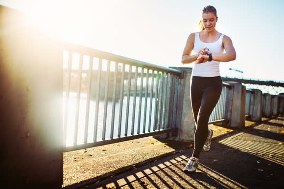 A woman jogging alongside a river checks her smartwatch.