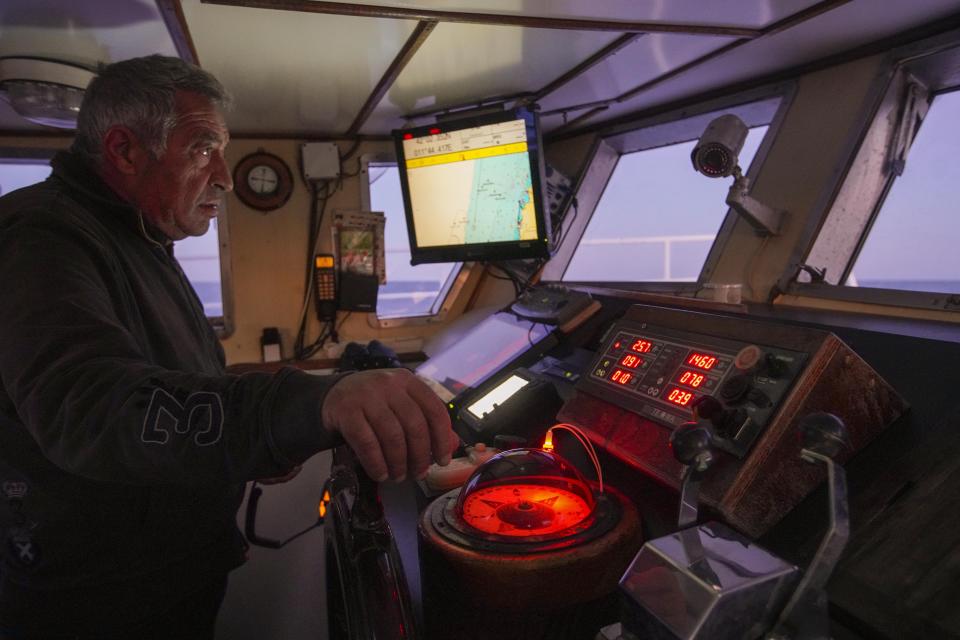 Pasquale Di Bartolomeo stands in the cockpit of his fishing trawler Marianna, during a fishing trip in the Tyrrhenian Sea, late Thursday, April 2, 2020. Italy’s fishermen still go out to sea at night, but not as frequently in recent weeks since demand is down amid the country's devastating coronavirus outbreak. For one night, the Associated Press followed Pasquale Di Bartolomeo and his crew consisting of his brother Francesco and another fishermen, also called Francesco, on their trawler Marianna. (AP Photo/Andrew Medichini)