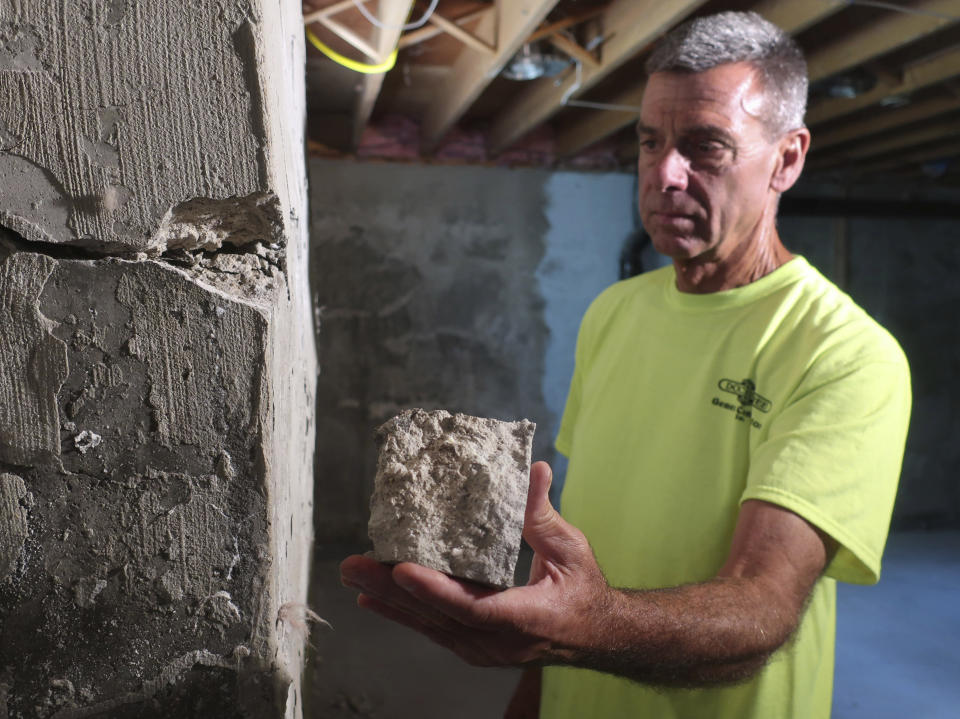 In this July 1, 2019 photo, contractor Don Childree holds a chunk of concrete pulled from the wall of a crumbling house foundation in Vernon, Conn. The concrete foundation is deteriorating due to the presence of an iron sulfide known as pyrrhotite, often described as "a slow-moving disaster," which causes concrete to crack and break gradually as it becomes exposed to water and oxygen. After worrying for years about the foundations crumbling beneath their houses, hundreds of suburban homeowners in a large swath of eastern Connecticut are getting help from the state to salvage their properties that had been doomed by bad batches of concrete. (AP Photo/Ted Shaffrey)