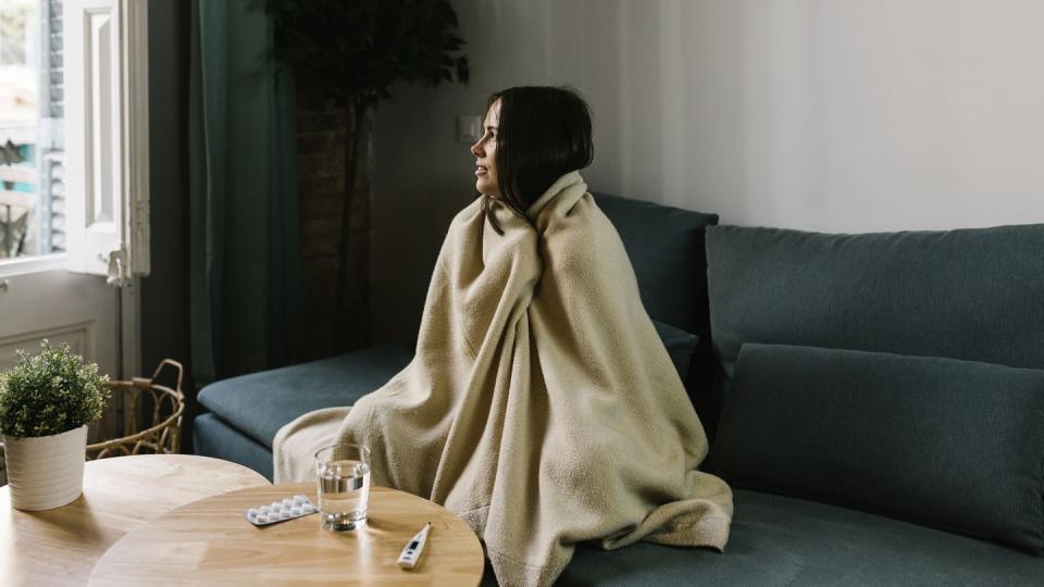 sick woman looking away while wrapped in blanket at home