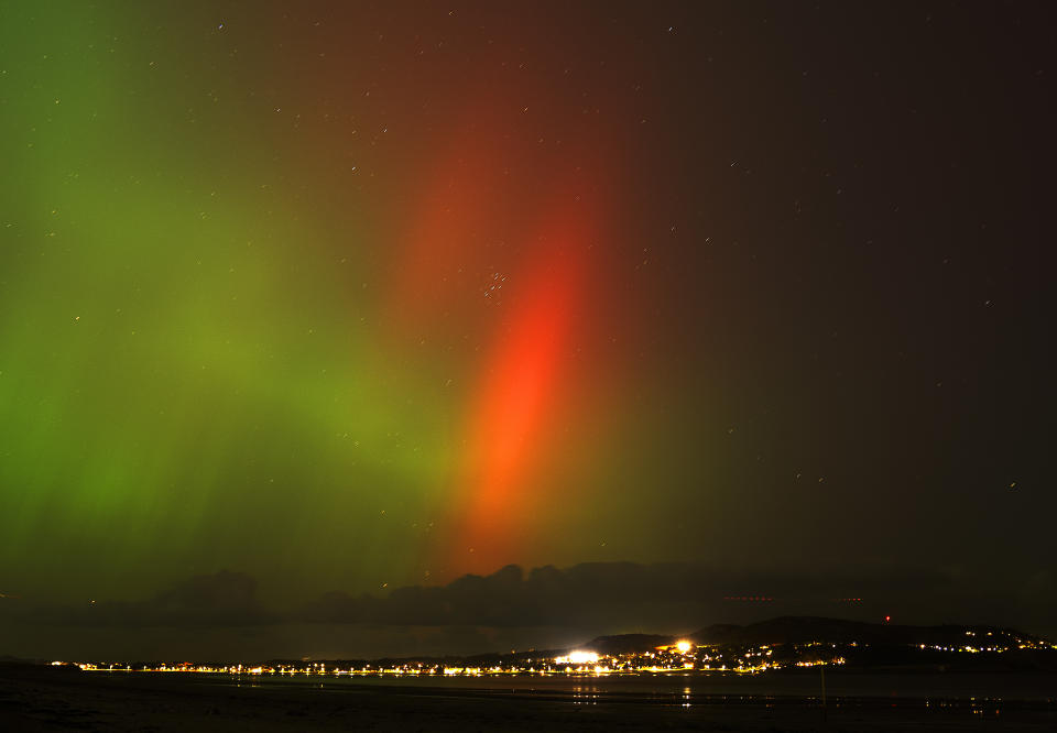 Northern lights over a coastal town with vibrant green and red auroras illuminating the night sky