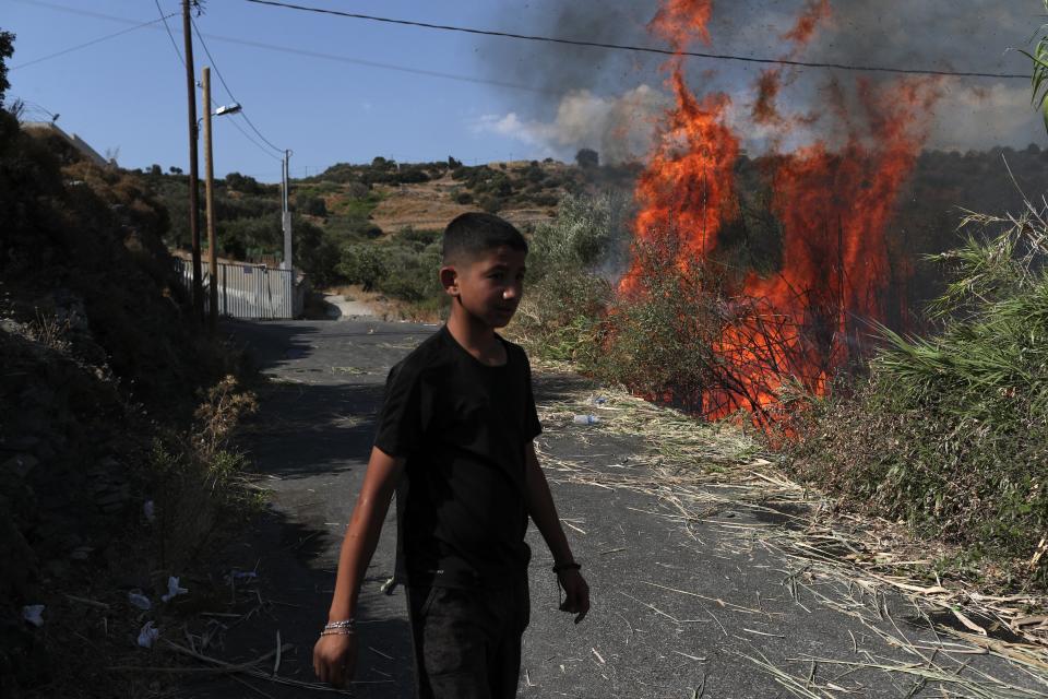 A migrant walks near a small fire in a field near Mytilene town, on the northeastern island of Lesbos, Greece, Saturday, Sept. 12, 2020. Thousands of asylum-seekers spent a fourth night sleeping in the open on the Greek island of Lesbos, after successive fires destroyed the notoriously overcrowded Moria camp during a coronavirus lockdown. (AP Photo/Petros Giannakouris)