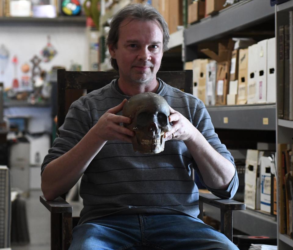 Kenyata Sullivan sits in the witch's chair from "The Conjuring" while holding a skull from "Sleepy Hollow" at his warehouse filled with Wilmington related movie memorabilia in Wilmington, N.C., Wednesday, February 23, 2022. Sullivan would like to one day open a museum that tells the story of the film industry in Wilmington.