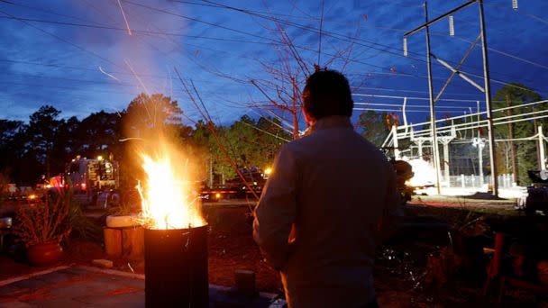 PHOTO: Gerardo Anicero warms himself in front of a makeshift fire as he watches Duke Energy personnel work to restore power at a crippled electrical substation in Carthage, N.C., on Dec. 4, 2022.  (Jonathan Drake/Reuters)