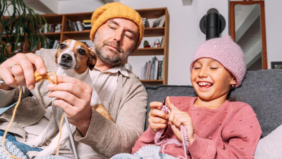 Padre e hijo tejiendo, con un perrito en el regazo