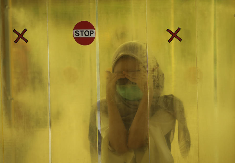 A woman reacts as she is sprayed with disinfectant inside a chamber as a precaution against the new coronavirus outbreak before entering a shopping mall in Jakarta, Indonesia, Tuesday, June 9, 2020. As Indonesia's overall virus caseload continues to rise, the capital city has moved to restore normalcy by lifting some restrictions this week, saying that the spread of the virus in the city of 11 million has slowed after peaking in mid-April. (AP Photo/Dita Alangkara)