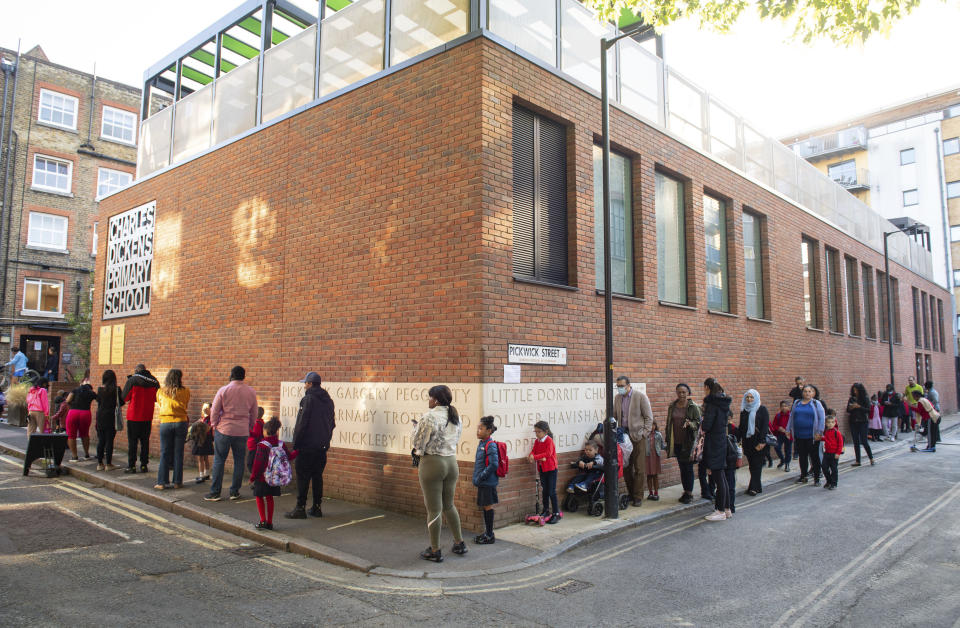 Pupils and parents queue on the first day back to school at Charles Dickens Primary School in London, Tuesday Sept. 1, 2020. Hundreds of thousands of British schoolchildren are heading back to classrooms, with the country watching nervously to see if reopening schools brings a surge in coronavirus infections. Tuesday marks the start of term for about 40% of schools in England and Wales, with the rest reopening in the coming days. (Dominic Lipinski/PA via AP)
