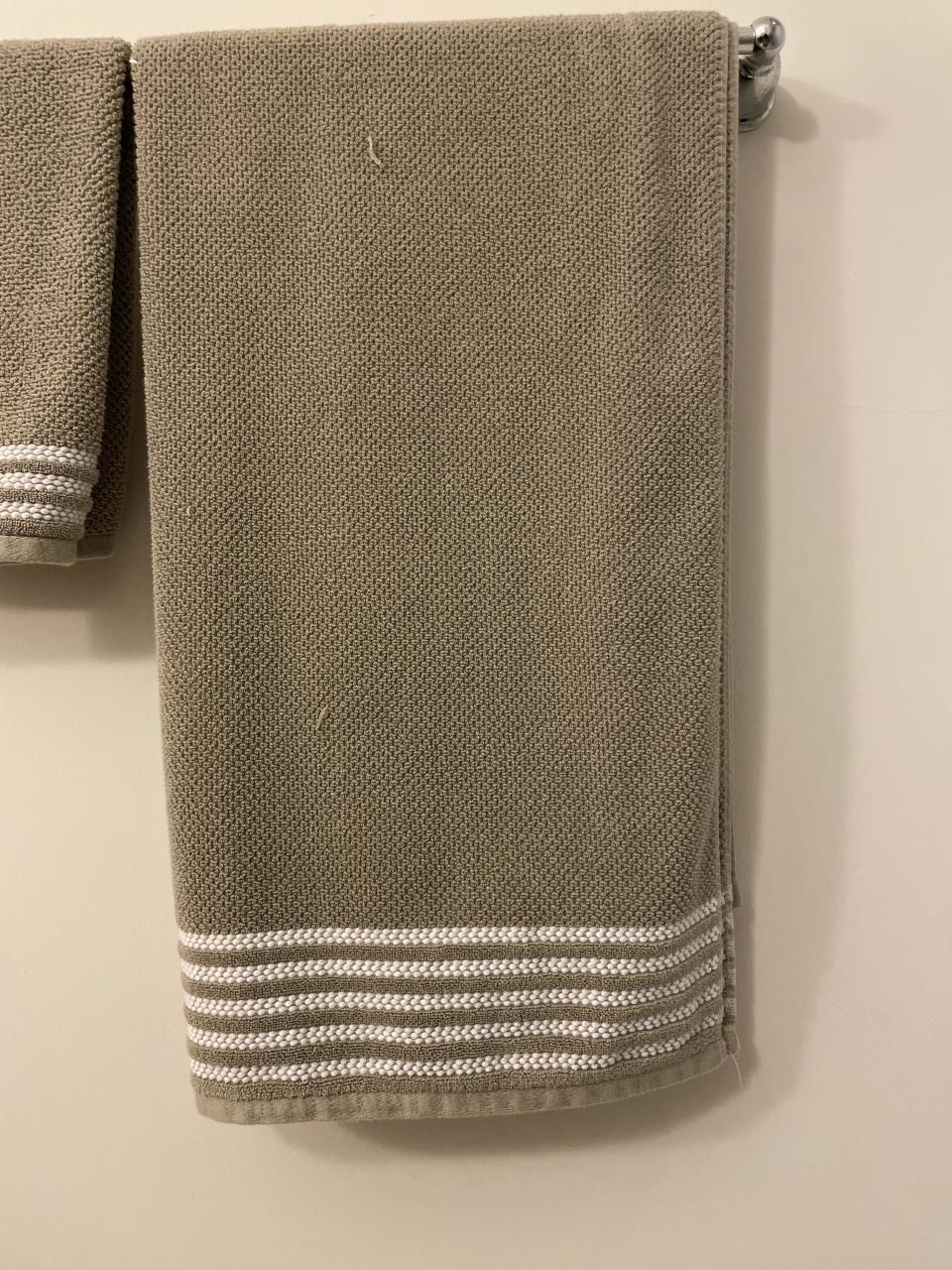 Beige towel hanging on a rack with decorative white stripes at the bottom