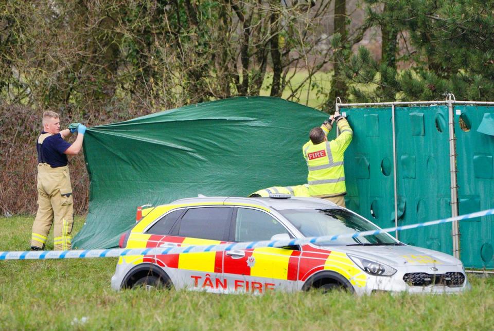 Firefighters erect screens at the scene in the St Mellons area of Cardiff where three people who disappeared on a night out died in a car crash (PA)