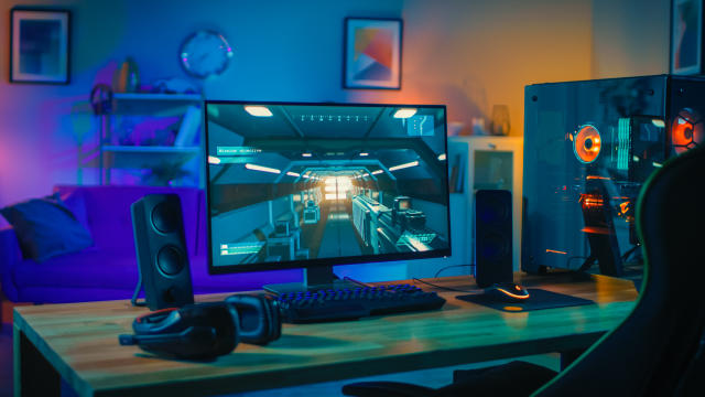 A gamer setup with blue and green neon lights. there are two xbox  controllers on the desk, one white and one black