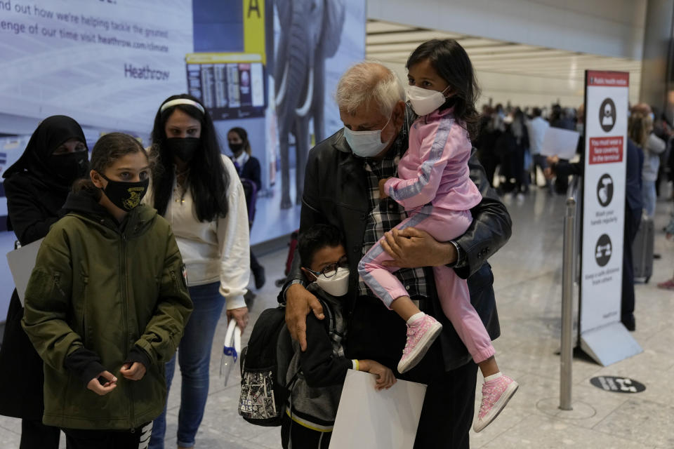 Members of the Mogul family are reunited as the grandfather carries his grandchildren, who arrived with their mother, third left, on a flight from Charlotte, North Carolina, in the U.S., at Terminal 5 of Heathrow Airport in London, Monday, Aug. 2, 2021. Travelers fully vaccinated against coronavirus from the United States and much of Europe were able to enter Britain without quarantining starting today, a move welcomed by Britain's ailing travel industry. (AP Photo/Matt Dunham)