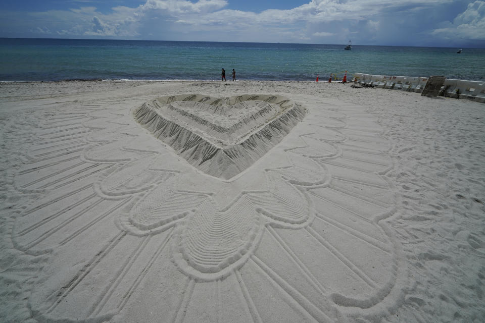 A giant heart sculpted from sand adorns the beach beside the area that is closed for search and rescue operations at the partially collapsed Champlain Towers South condo building, Friday, July 2, 2021, in Surfside, Fla. (AP Photo/Gerald Herbert)