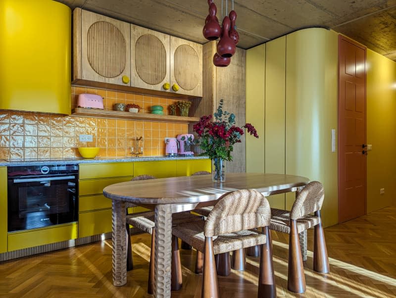 Yellow kitchen with fluted wood cabinets, parquet floor, window bar and dining table