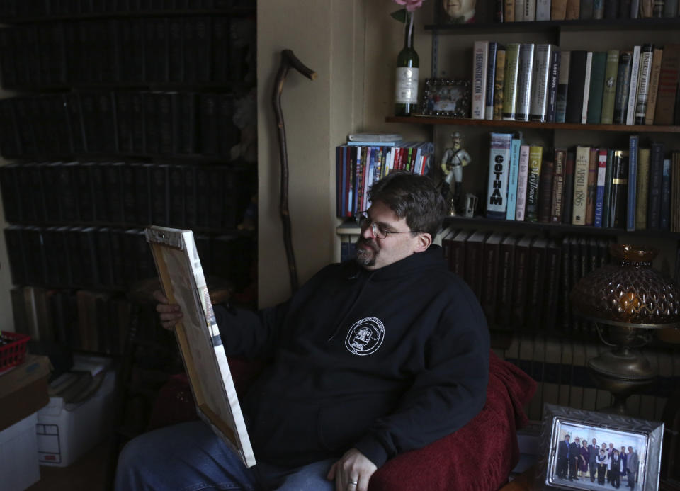 Brian Walter smiles as he looks at a photograph of his late father at his home in the Queens borough of New York, Wednesday, April 7, 2021. Walter, deemed an essential worker during the pandemic as a New York City Transit employee, did most of the grocery shopping and errand running for his family and worries that he may have infected his father. John Walter died of COVID-19 on May 10, 2020. (AP Photo/Jessie Wardarski)