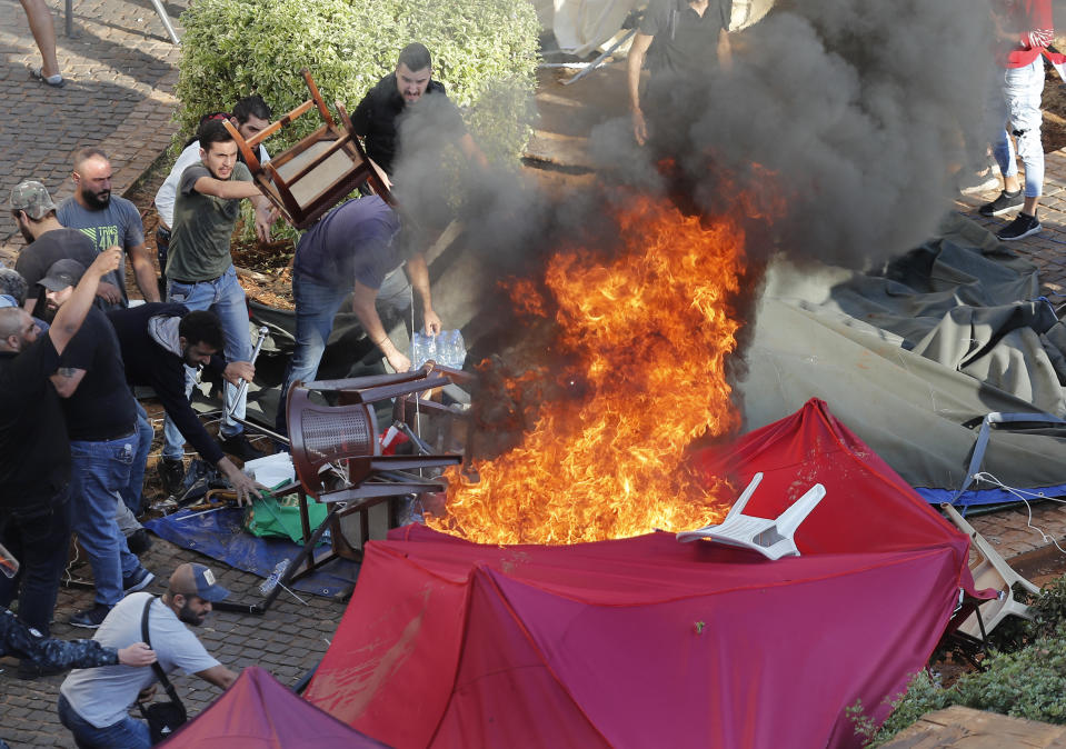 FILE - In this Tuesday, Oct. 29, 2019 file photo, supporters of the Shiite Hezbollah group burn tents in the camp set up by anti-government protesters near the government palace, in Beirut, Lebanon. Lebanon’s protests have brought out people from across the country’s spectrum of faiths and communities trying to throw out the entire ruling elite. They give a glimpse into a Lebanon transcending longtime divisions among Muslims, Christians and other sects. (AP Photo/Hussein Malla, File)