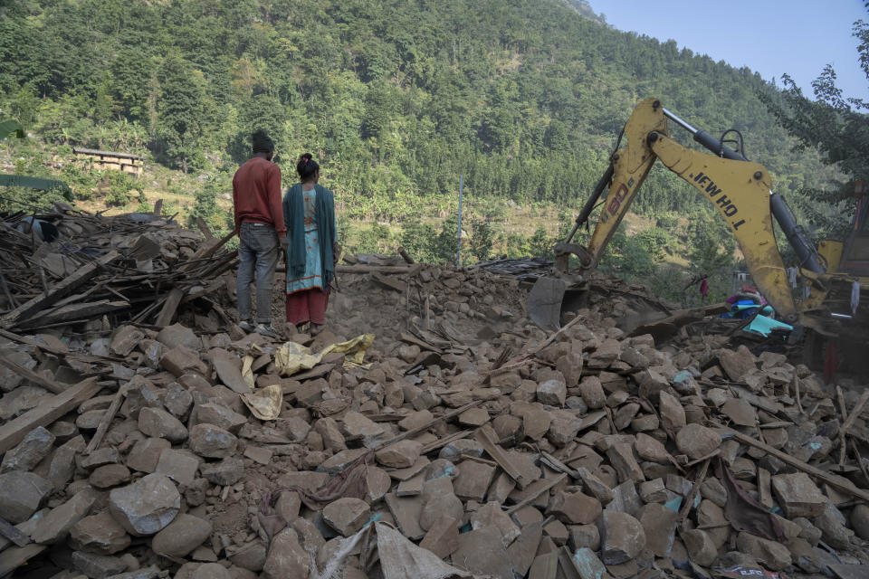 Survivors watch an excavator clear debris of earthquake damaged houses as they look for their belongings in Rukum District, northwestern Nepal, Monday, Nov. 6, 2023. The Friday night earthquake in the mountains of northwest Nepal killed more than 150 people and left thousands homeless. (AP Photo/Niranjan Shrestha)