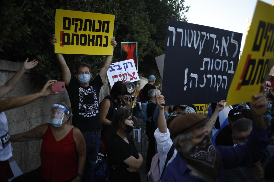 Protesters, defying orders to maintain social distancing requirements, chant slogans outside of the Prime Minister's residence in Jerusalem, Tuesday, July 14, 2020. Thousands of Israelis demonstrated outside the official residence of Prime Minister Benjamin Netanyahu, calling on the embattled Israeli leader to resign as he faces a trial on corruption charges and grapples with a deepening coronavirus crisis. The signs read: "No to dictatorship under the shelter of the Coronavirus," and "you are detached. We are fed up." (AP Photo/Ariel Schalit)