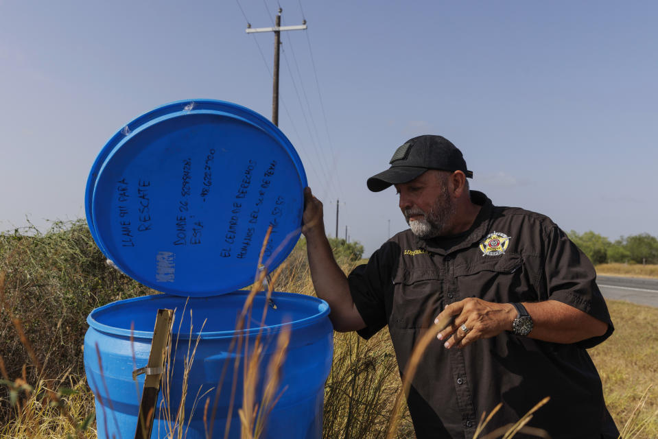 Jim Hogg County Sheriff's Investigator Ruben Garza inspects a water station for immigrants containing sealed jugs of fresh water along a fence line near a roadway in rural Jim Hogg County, Texas, Tuesday, July 25, 2023. The South Texas Human Rights Center maintains over 100 blue barrels consistently stocked with water across rural South Texas to serve as a life-saving measure for immigrants who have crossed into the United States to travel north in the sweltering heat. (AP Photo/Michael Gonzalez)