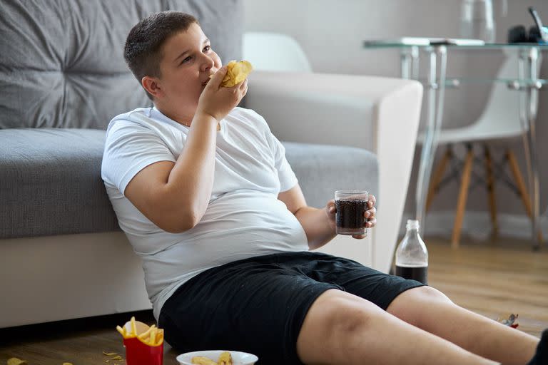 fat overweight teenager boy has bad nutrition, eat unhealthy food. sit on the floor eating junk food and watching tv