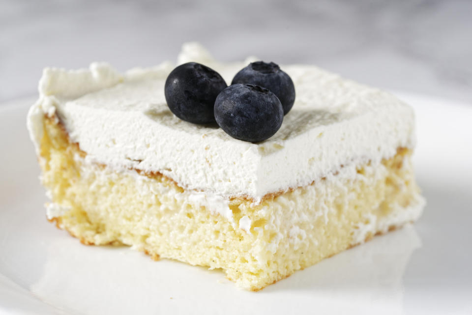 A slice of cake with vanilla frosting and blueberries.