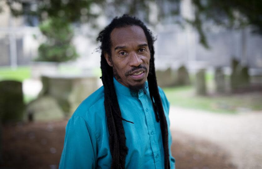 Benjamin Zephaniah with long dreadlocks in a bright blue shirt posing for photos in an outdoor courtyard