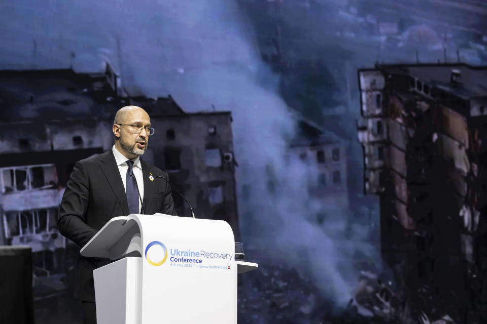 Ukrainian Prime Minister Denys Shmyhal speaks with footage from the war projected on screen during a plenary session at the Ukraine Recovery Conference URC, Monday, July 4, 2022 in Lugano, Switzerland. The URC is organised to initiate the political process for the recovery of Ukraine after the attack of Russia to its territory. (Alessandro della Valle/Keystone via AP)