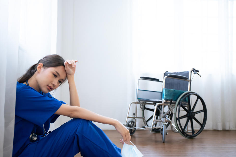 Tired female nurse wears face mask blue uniform sits on hospital floor