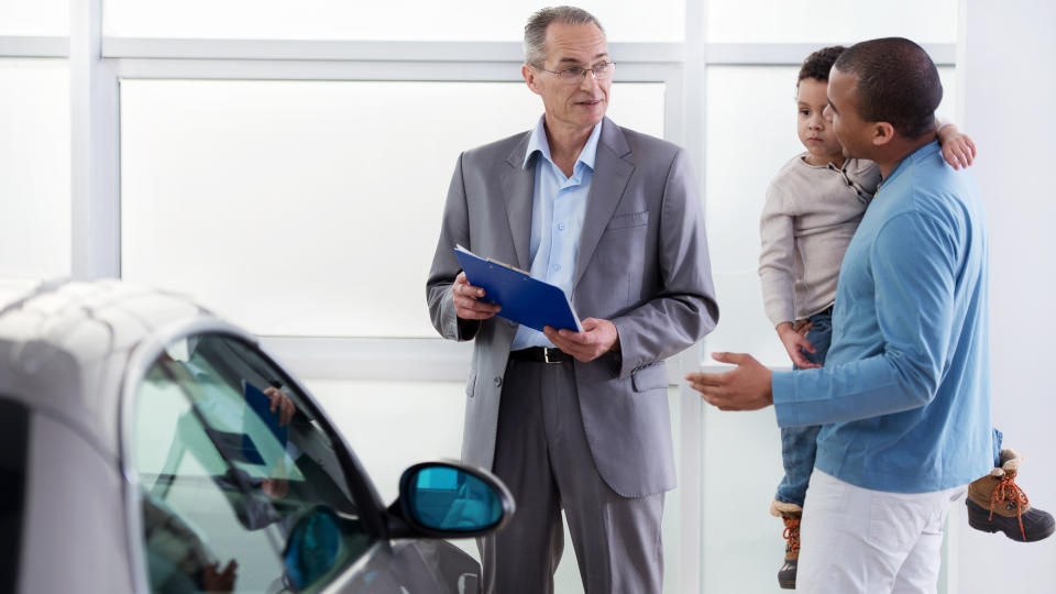 Smiling African American father holding his little boy and talking to the car salesperson and buying a new car.