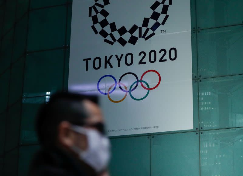 A man wearing a protective face mask following an outbreak of the coronavirus disease (COVID-19) walks past a banner for the upcoming Tokyo 2020 Olympics in Tokyo