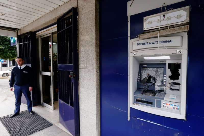 A security guard stands near a damaged ATM machine outside BBAC bank in Beirut