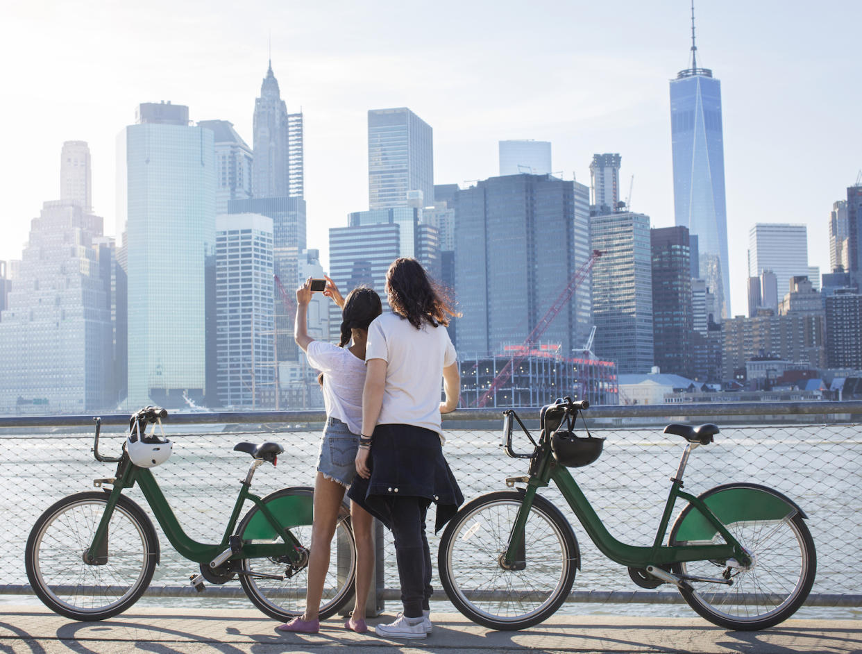 A climate change-con couple takes a selfie along a river with buildings in the central business district in the background