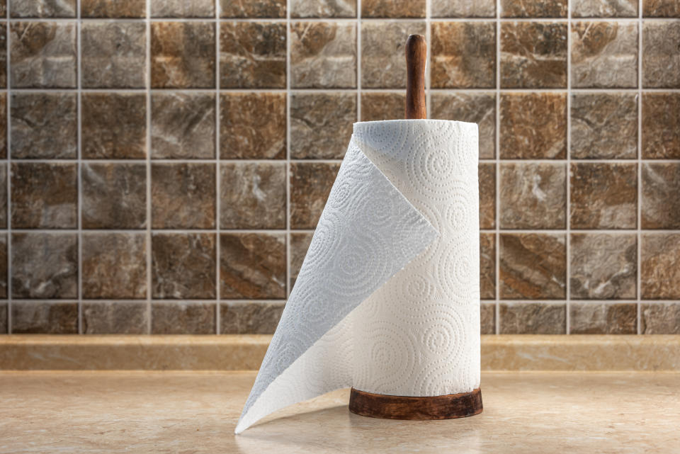 A paper towel roll on a wooden holder is displayed on a kitchen countertop with a tiled backsplash