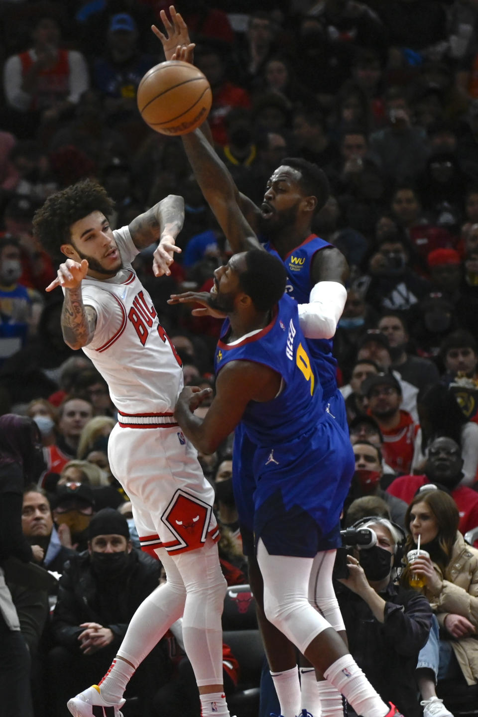 Chicago Bulls guard Lonzo Ball, left, passes the ball away from Denver Nuggets forward JaMychal Green, back, and guard Davon Reed (9) during the first half of an NBA basketball game, Monday, Dec. 6, 2021, in Chicago. (AP Photo/Matt Marton)