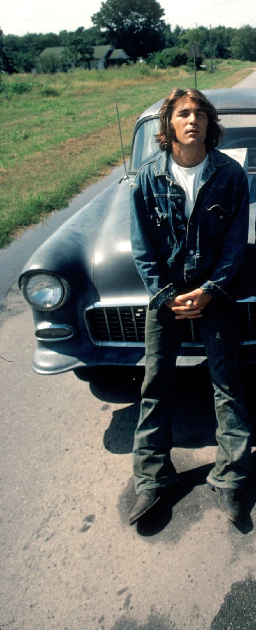 the mechanic leans against his vintage muscle car